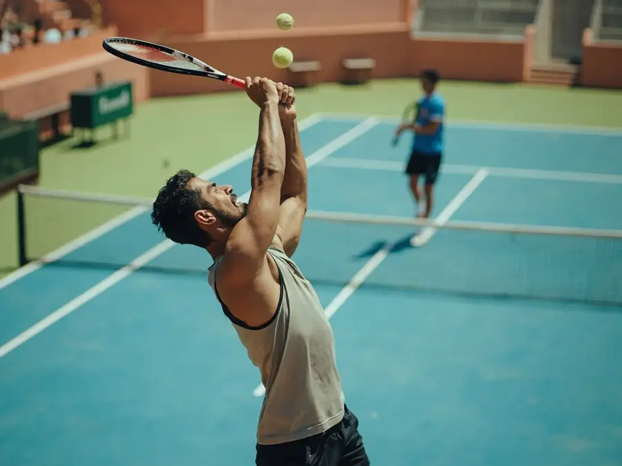 Indian male tennis player at the peak of a serve toss on outdoor hardcourt